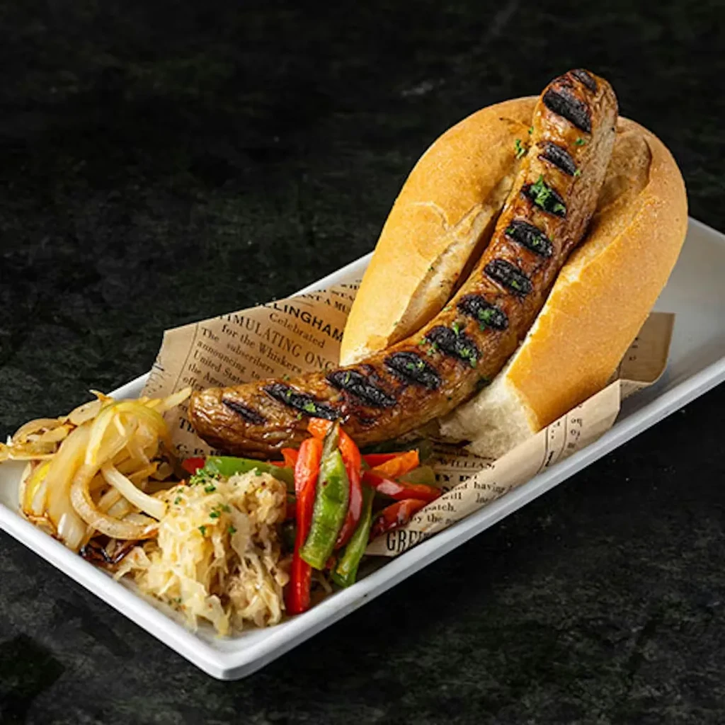Grilled sausage in bun with caramelized onions, sauerkraut, bell peppers.