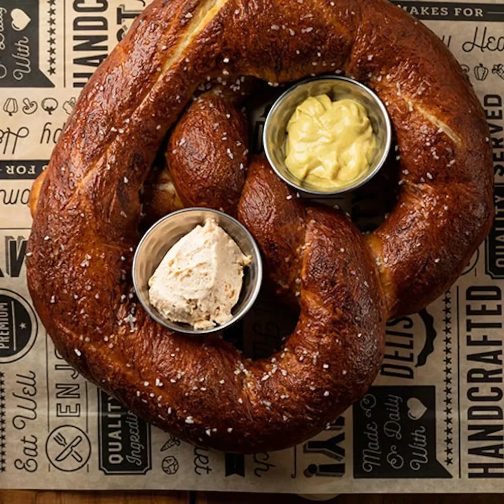 Salted, golden-brown pretzel and two dips on patterned paper.