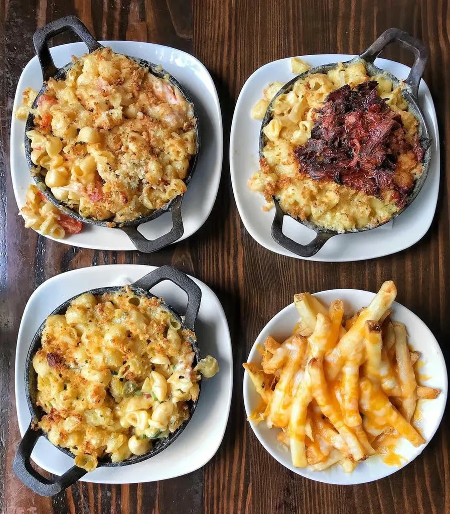 Three mac and cheese dishes and cheese fries on a rustic table.