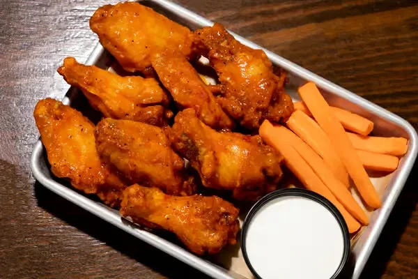 Buffalo chicken wings, carrot sticks, white dipping sauce on a metal tray.