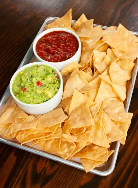 Crispy tortilla chips, chunky red salsa, and green guacamole on a tray.