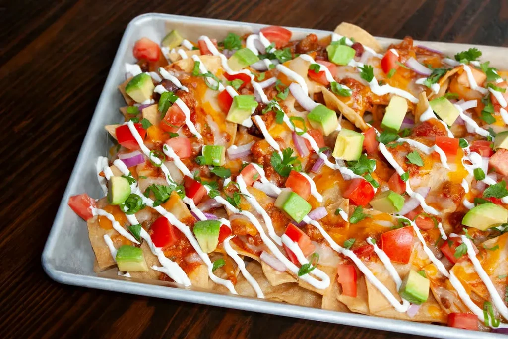 Rectangular metal tray of nachos with melted cheese, avocado, and sour cream.