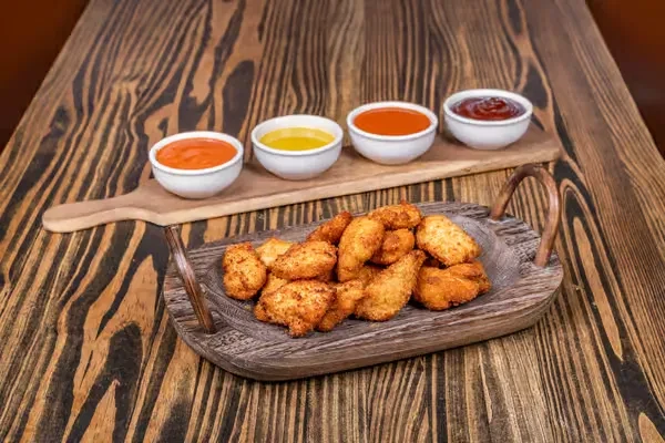 Crispy chicken nuggets and four sauces on rustic wood.