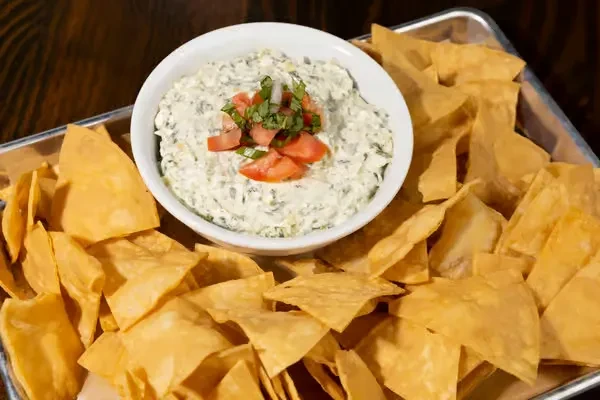 Close-up of spinach or artichoke dip with tomatoes, herbs, and tortilla chips.