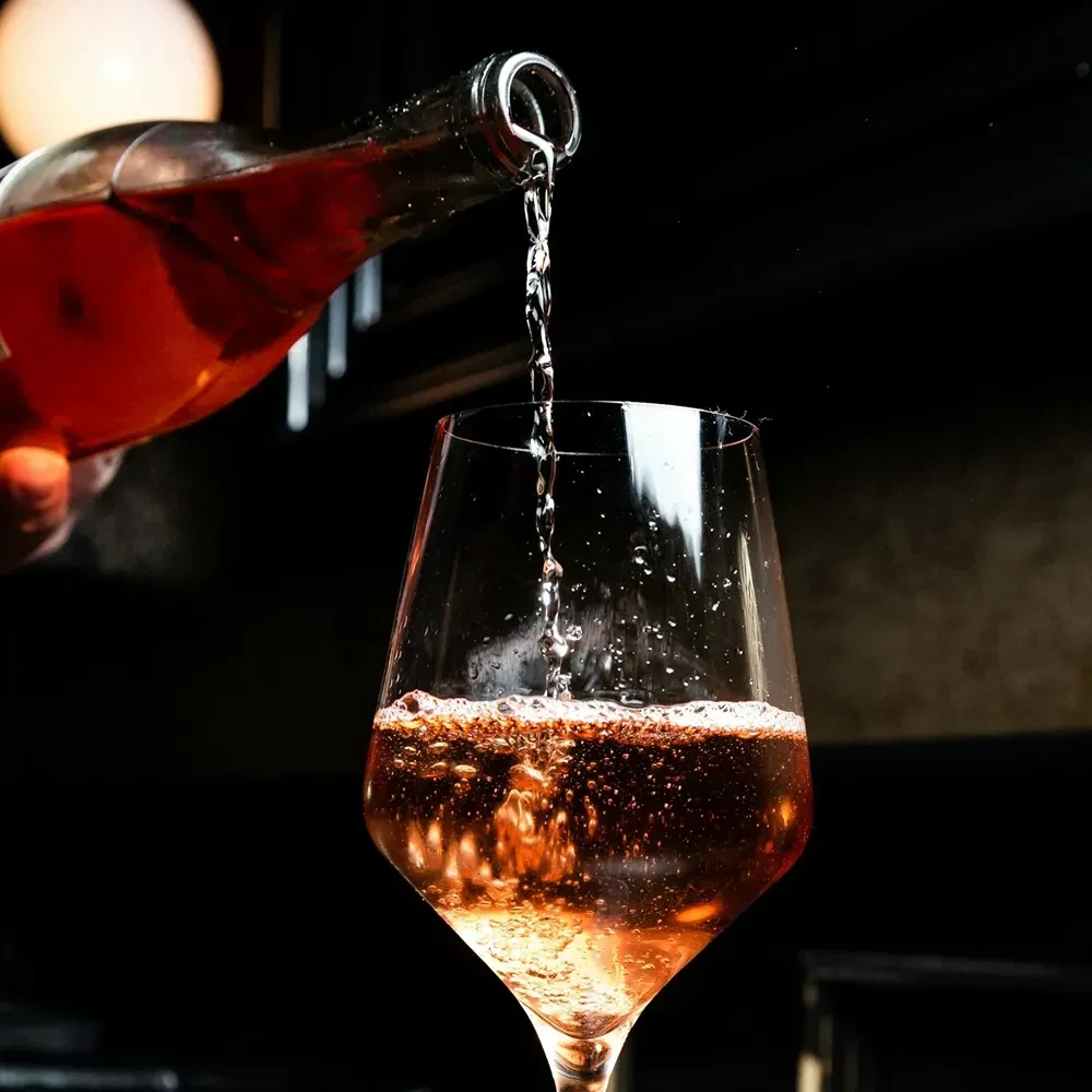 Light-colored wine pours from a bottle into a glass, splashing.