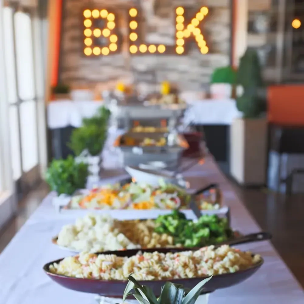 Restaurant buffet table with salads, hot food, and illuminated "BLK" sign.