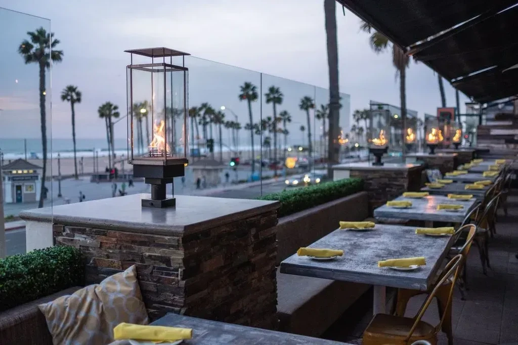 Restaurant patio at dusk with warm flame pillars overlooking a beach.