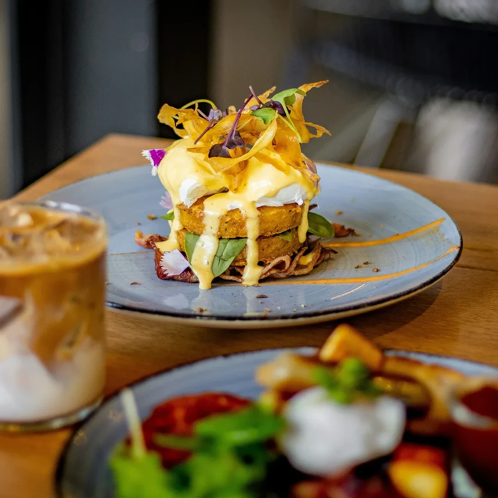 Artfully plated stacked Eggs Benedict with Hollandaise and iced coffee.