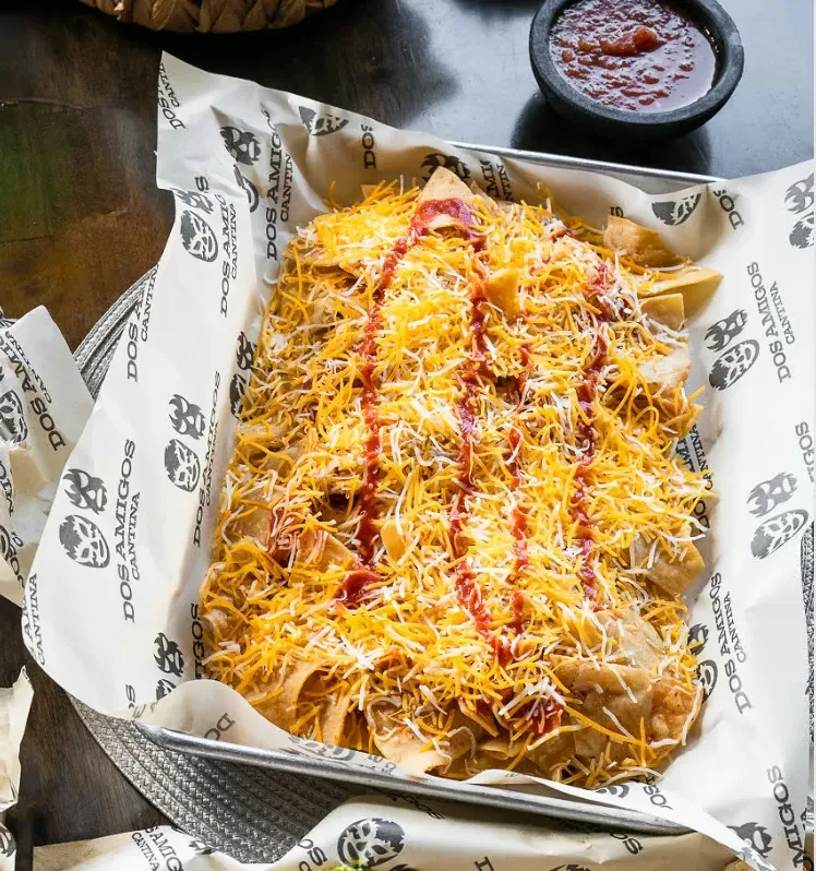 Nachos with melted cheese, red sauce, and salsa in a branded tray.