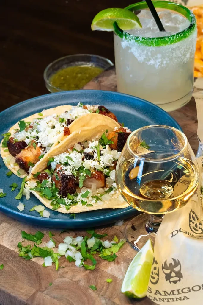 Grilled street tacos, tequila, and a lime margarita on a wooden surface.