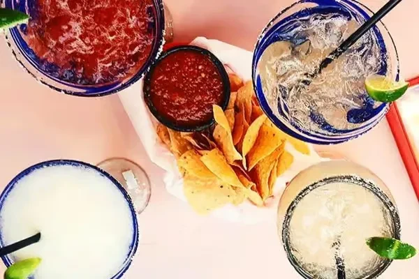 Overhead view of four garnished margaritas, tortilla chips, and red salsa.