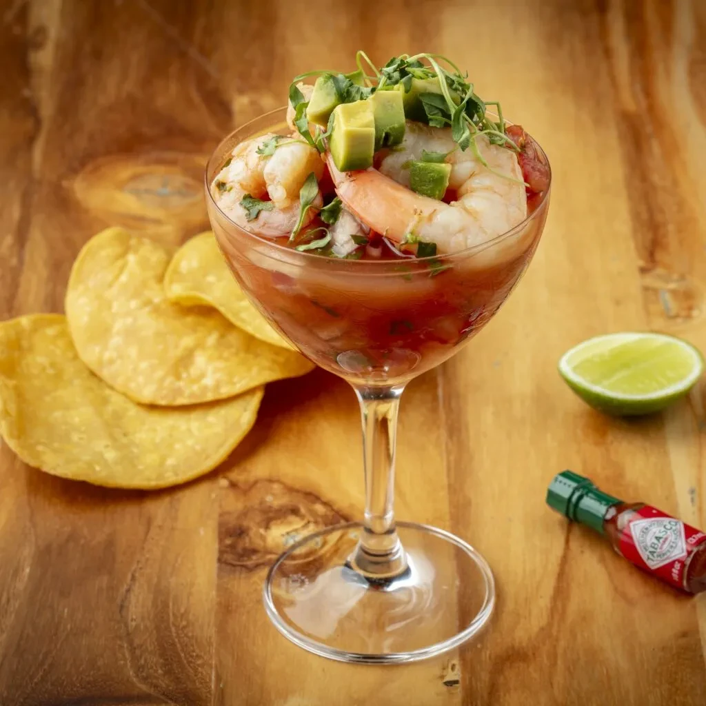 Shrimp cocktail in glass with avocado, chips, lime, and hot sauce.