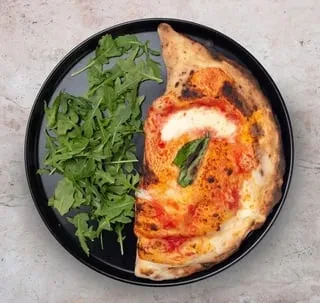 Golden-brown calzone with tomato, mozzarella, basil, and arugula salad.