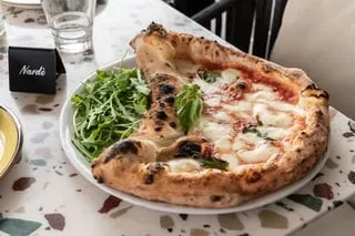 Neapolitan Margherita pizza with arugula and "Nardè" sign on a terrazzo table.