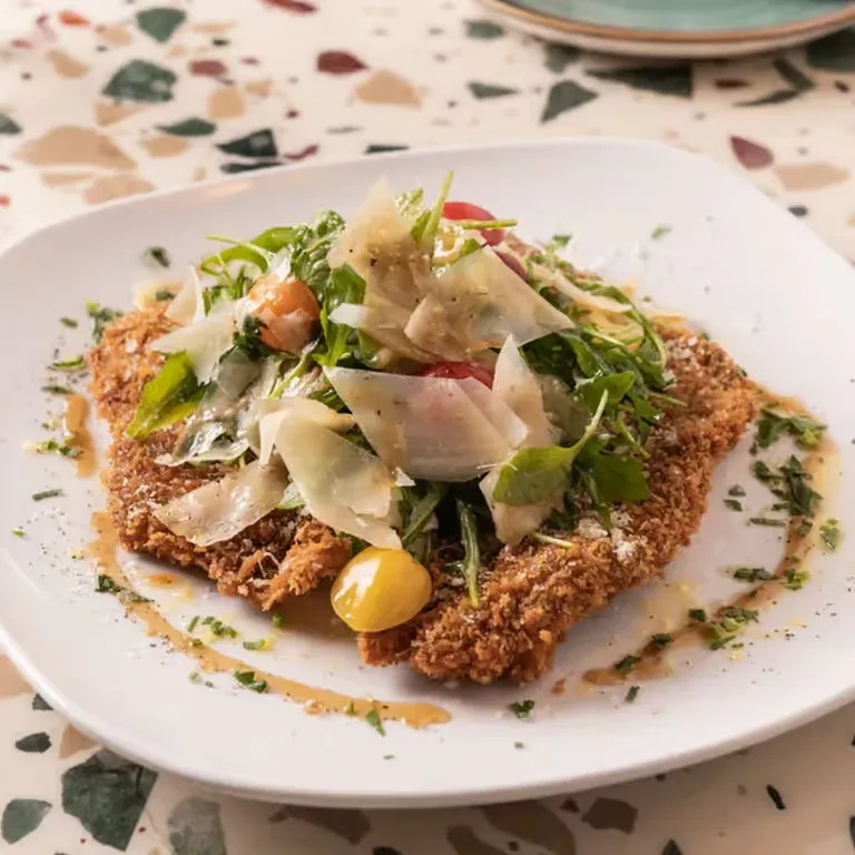Plated golden-brown cutlet topped with green salad, Parmesan, and cherry tomatoes.