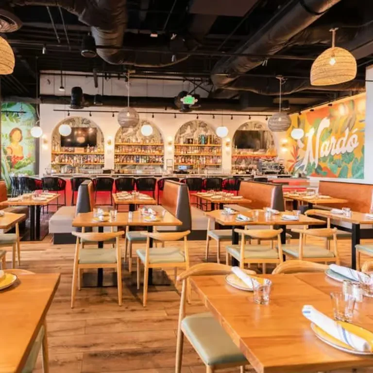 Empty, modern restaurant interior with a bar, wood tables, and vibrant murals.