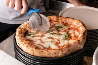 Person slices a freshly baked pizza with a charred, puffy crust.