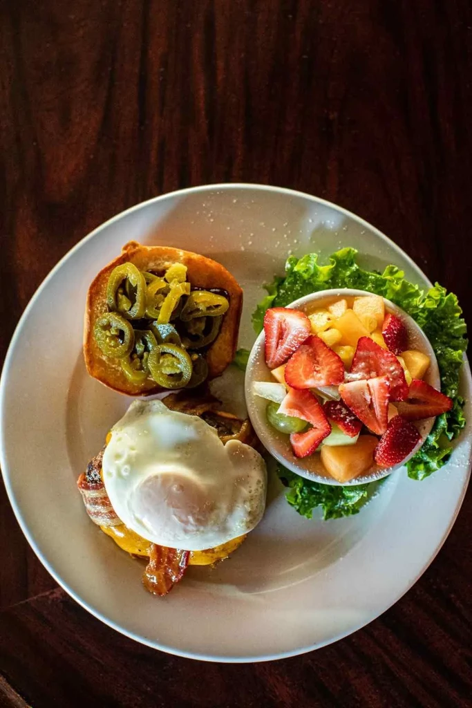 Close-up: breakfast plate with egg, bacon, jalapeño sandwich and fruit.