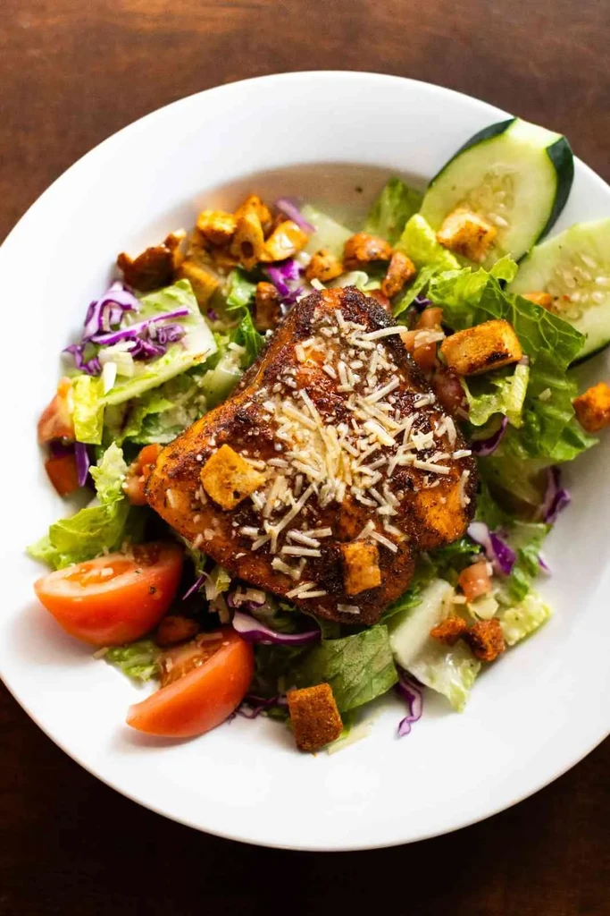 Overhead salad with seared protein, lettuce, tomatoes, cheese, croutons.