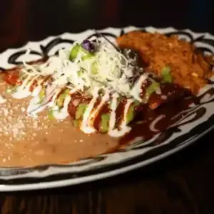 Plate of sauced enchiladas, refried beans, and rice, garnished with cheese.