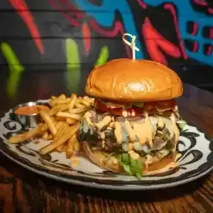 Gourmet burger, fries, and sauce on a decorative plate with graffiti background.