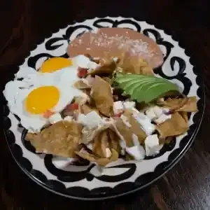 Colorful breakfast plate with eggs, chilaquiles, avocado, and refried beans.