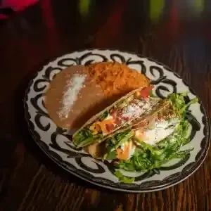 Two generously filled tacos, refried beans, on a decorative plate.