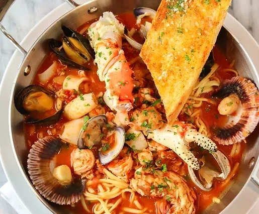 Overhead, close-up seafood pasta with crab, mussels, shrimp, garlic bread.