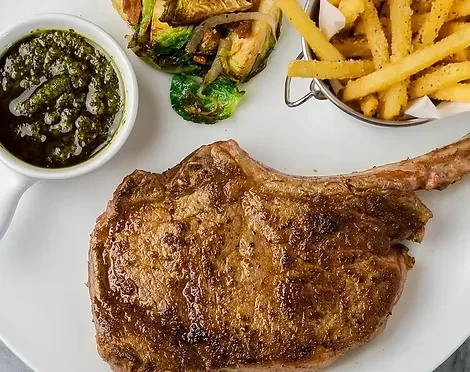Grilled bone-in steak, Brussels sprouts, green sauce, and french fries.