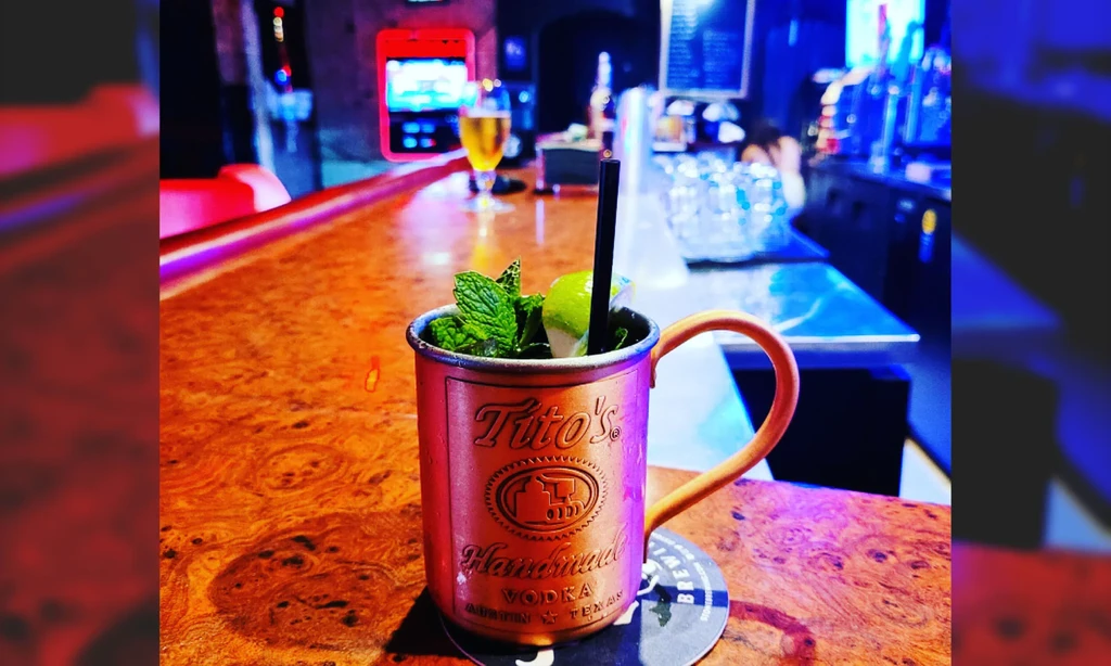 Copper mug with Tito's vodka text, mint, and lime on a bar.