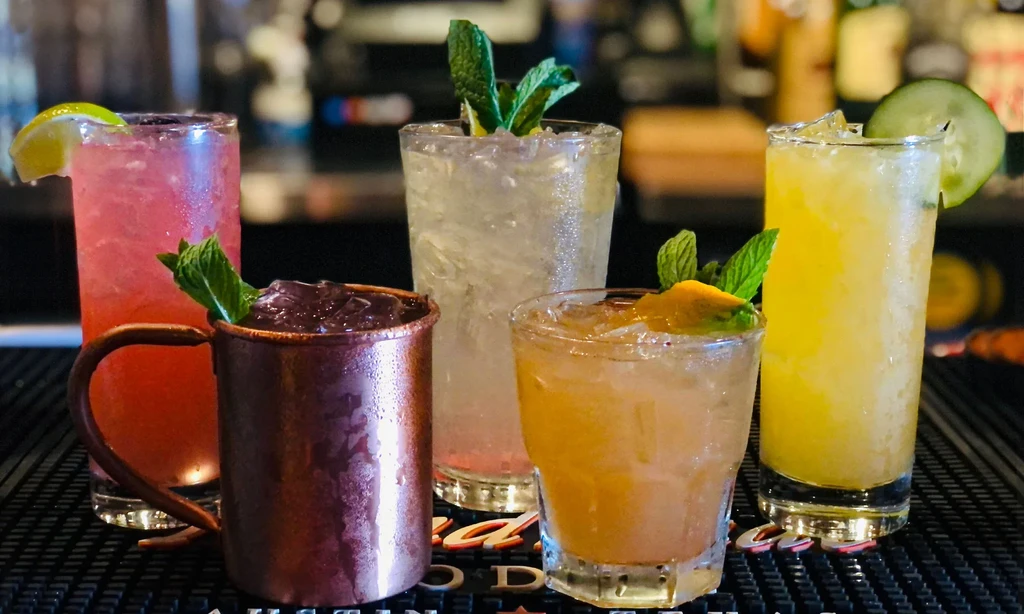 Five cold, garnished cocktails on a bar mat, "Austin Texas" visible.