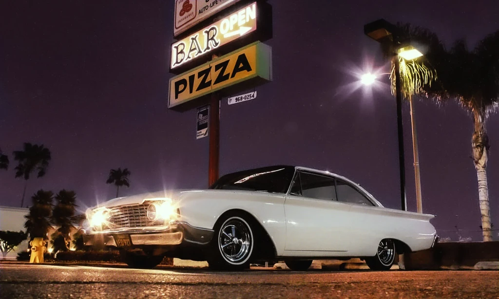 Classic white American car at night near a "BAR OPEN PIZZA" sign.