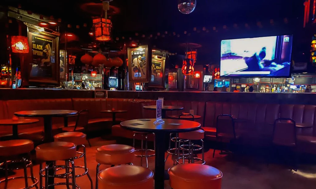 Red-lit, retro bar interior with banquettes, tables, and a disco ball.