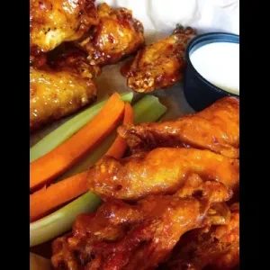 Top-down view of glazed chicken wings, carrots, celery, and dip.