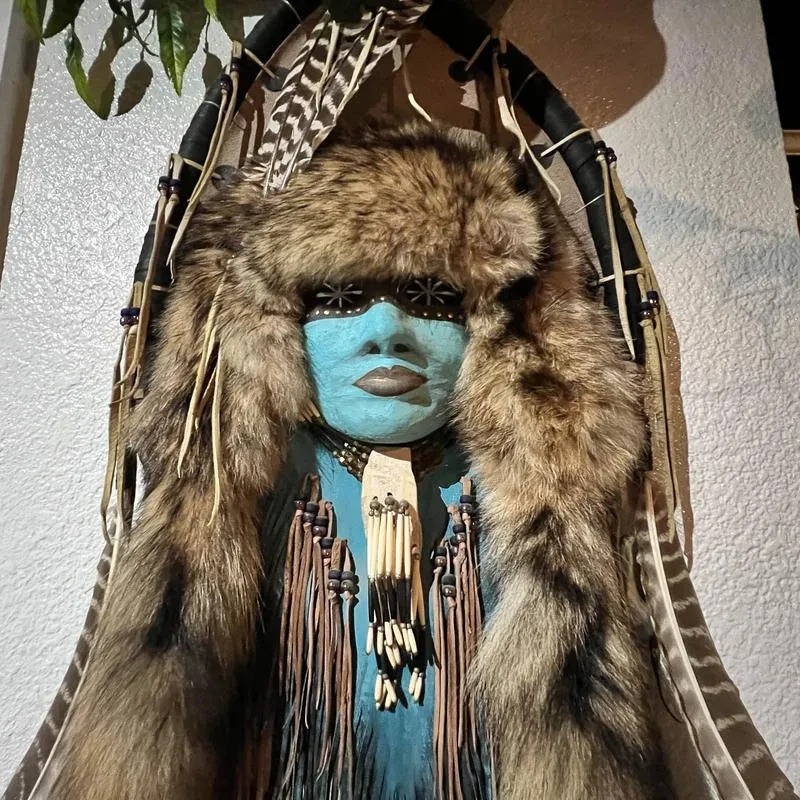 Elaborate blue face mask with shaggy fur, feathers, and bone ornaments.