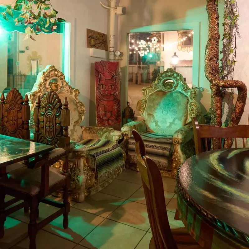 Eclectic restaurant interior with ornate furniture, cat sculpture, and green-blue lighting.