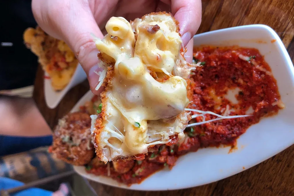 Broken fried mac and cheese ball reveals gooey, stretching cheese.