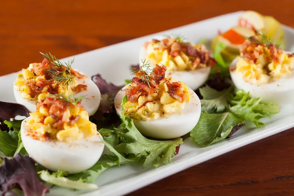 Deviled eggs with bacon, dill, and red seasoning on fresh greens.