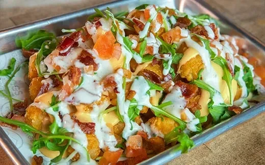 Loaded tater tots with bacon, tomatoes, arugula, and two sauces.