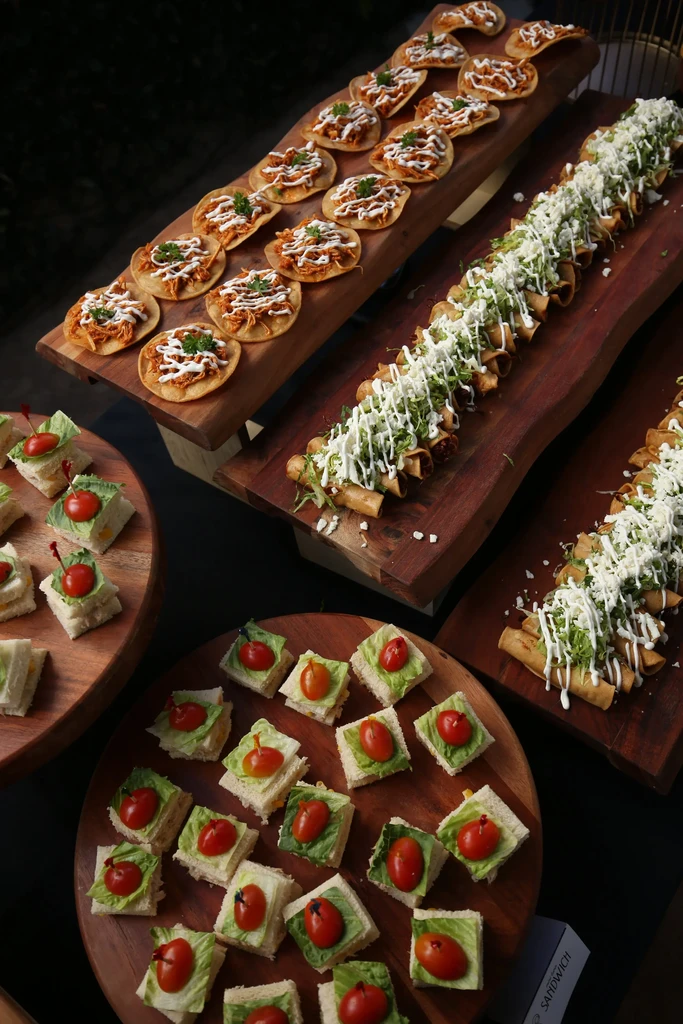Catering spread of tostadas, taquitos, and mini sandwiches on wooden boards.