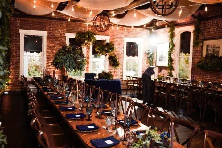 Warmly lit dining hall with long tables, brick walls, and draped canopy.