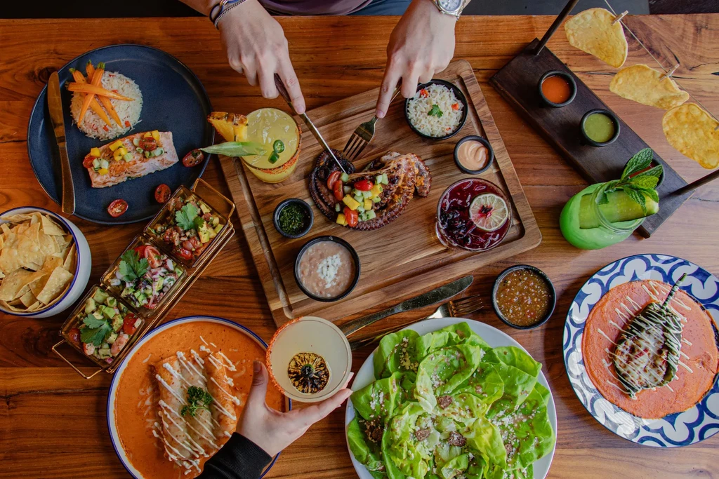 Vibrant overhead view of diverse dishes and cocktails on a restaurant table.