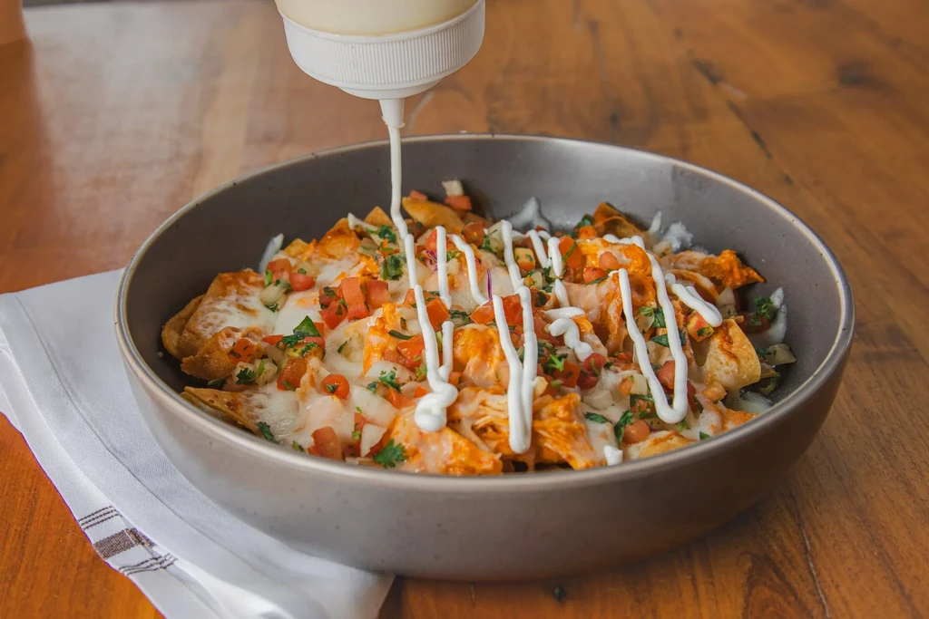 Nachos with melted cheese, chicken, tomatoes, herbs, and drizzled sour cream.
