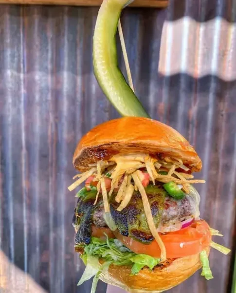 Tall, skewered burger with patty, cheese, veggies, and crispy toppings.