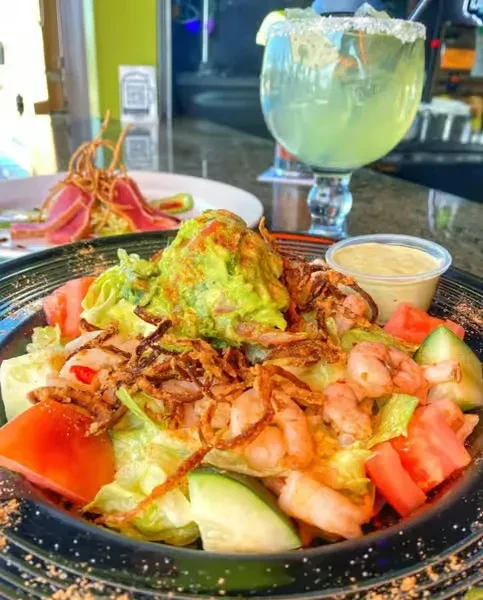 Close-up of shrimp salad with guacamole, margarita, and blurred tuna dish.