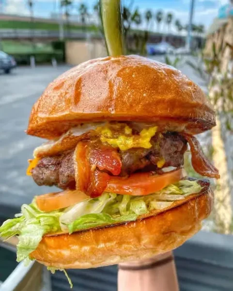 Close-up of a gourmet burger with bacon, egg, cheese, and pickle skewer.