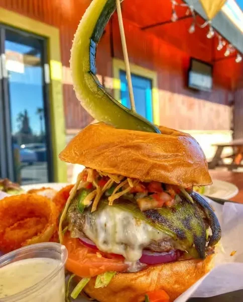 Gourmet burger with melted cheese, grilled peppers, onion rings, and pickle.