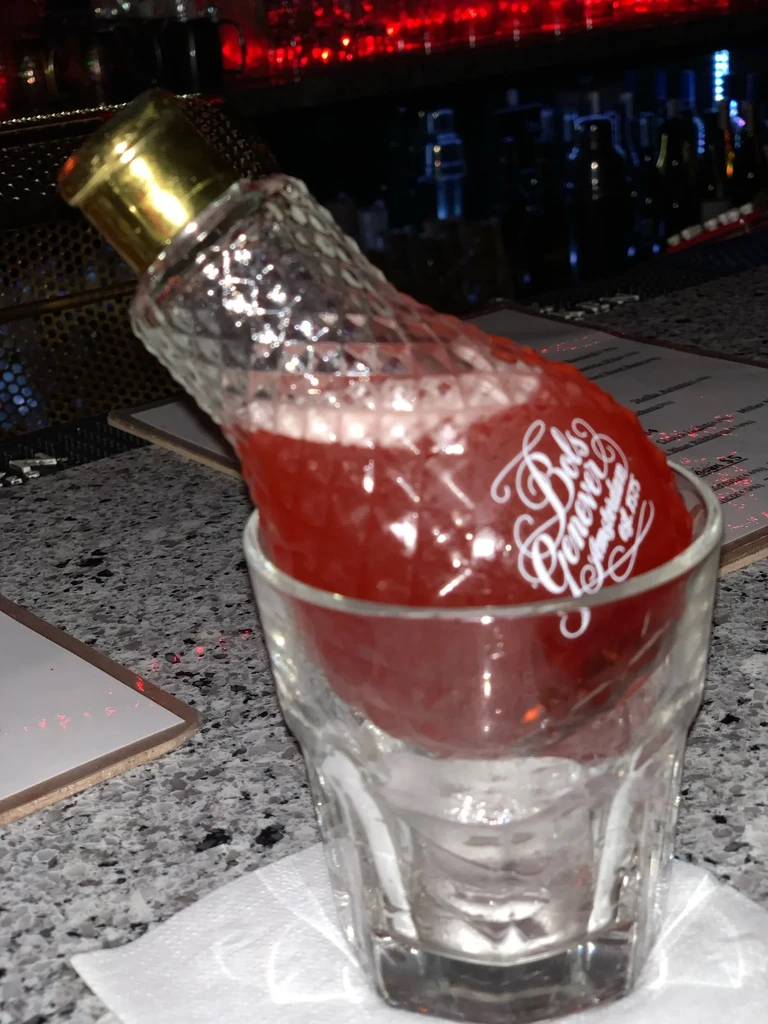 Red Bols Genever cocktail in a small bottle nested in a tumbler.