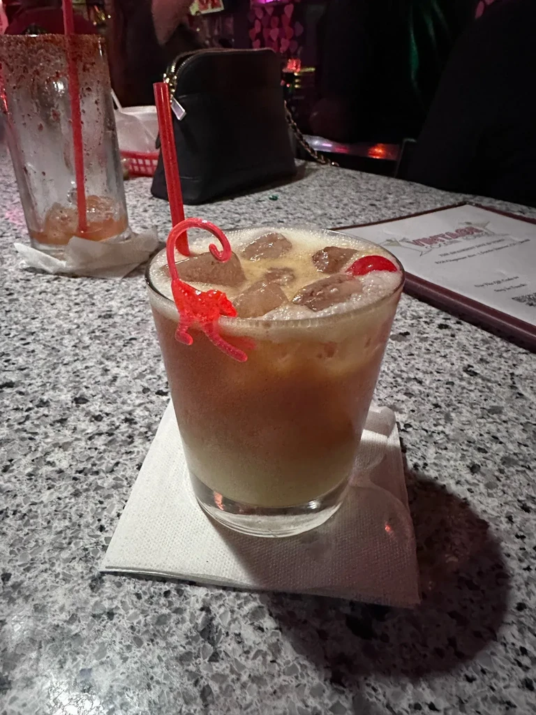 Layered drink with red cherries and a red monkey stir stick.