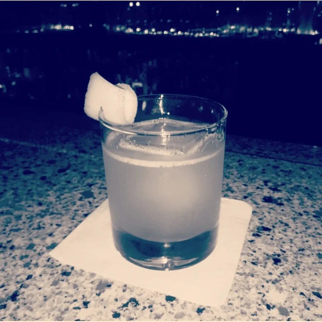 Close-up of an amber cocktail with lemon twist on a bar counter.